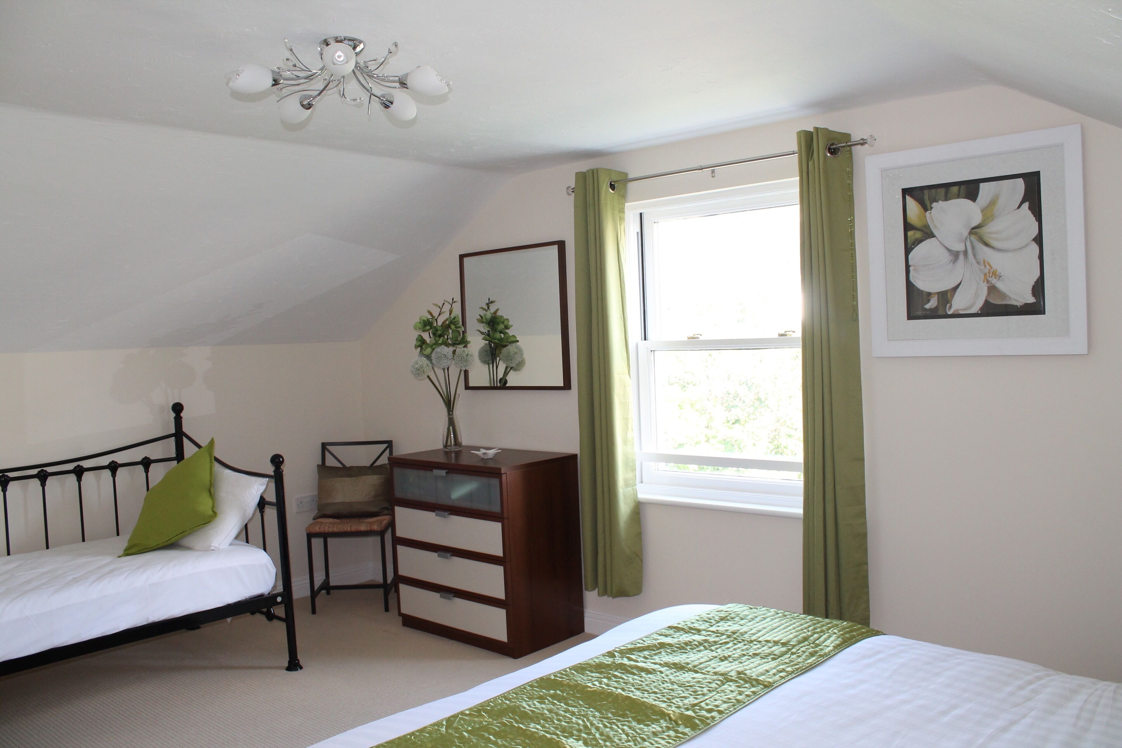 A bedroom with a bed, a dresser, a chair, a desk, a window with curtains, a ceiling light, and a framed picture on the wall.