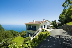 A two-story house with a balcony, a stone retaining wall, and a view of the sea. - BEAUTIFUL BASQUE HOUSE WITH MAGNIFICENT VIEWS. (Getaria)
