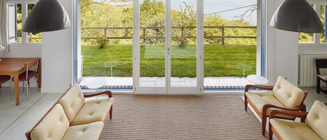 Una habitación amplia con un gran ventanal corredero que da a un jardín. Hay dos sillas y una mesita en la habitación.