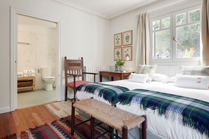 A bedroom with a bed, a wooden chair, a small table with a plant, and a window with curtains. - BEAUTIFUL BASQUE HOUSE WITH MAGNIFICENT VIEWS. (Getaria)