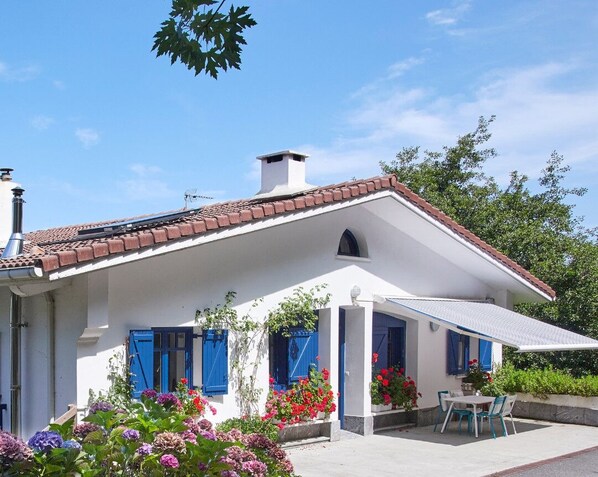 A white building with a red-tiled roof, blue shutters, and a covered patio area with a table and chairs. - BEAUTIFUL BASQUE HOUSE WITH MAGNIFICENT VIEWS. (Getaria)