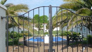 Ein durch eine Mauer abgegrenzter Bereich mit Pool, Palmen und einem Gebäude im Hintergrund.