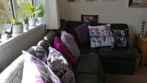 Ein Wohnzimmer mit einem dunkelbraunen Ledersofa, mehreren Kissen und einem Fenster mit Blumentöpfen.