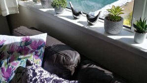 Blick aus dem Fenster auf ein rosafarbenes Gebäude, einen Swimmingpool und verschiedene Blumentöpfe auf einem Fensterbrett.