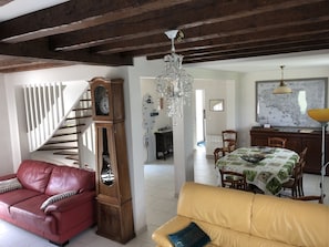 A spacious living area with a red leather sofa, a yellow sofa, a wooden grandfather clock, a chandelier, a dining table with chairs, and a kitchen area with a marble backsplash. - House with lovely garden (Pénestin)