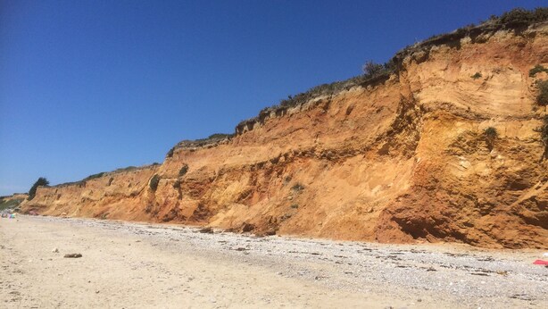 Eine Küstenlandschaft mit einem Sandstrand und einer steilen Klippe.