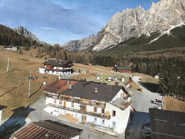Un pueblo de montaña con edificios tradicionales, una plaza central y montañas al fondo.