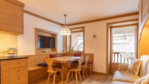 A cozy room with a wooden dining table, chairs, a TV mounted on the wall, and a window with curtains.