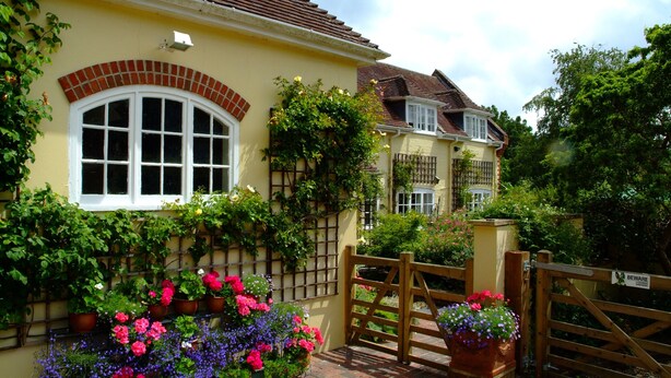 Ein gelbes Haus mit Bogenfenster aus Ziegeln, einem Holztor und Kübelblumen.