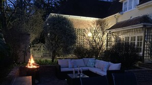 Eine Terrasse im Freien mit Terrakottafliesen, einem Feuerkorb, einer Sitzecke und einem Tisch mit Gläsern.