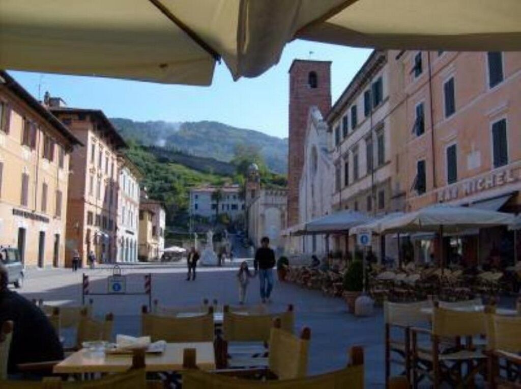 Un café al aire libre con mesas y sillas, rodeado de edificios históricos y una montaña al fondo.