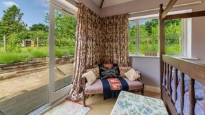 A room with a sliding glass door leading to a garden, a cushioned bench with pillows, and a wooden headboard. - Apple Tree Barn, Langham, Norfolk (Langham)