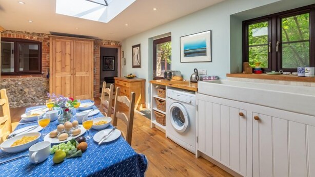 A bright kitchen with a skylight, wooden cabinets, a washing machine, and a dining area set for breakfast. - Apple Tree Barn, Langham, Norfolk (Langham)