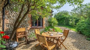 An outdoor seating area with a stone wall, wooden chairs, and a grill. - Apple Tree Barn, Langham, Norfolk (Langham)
