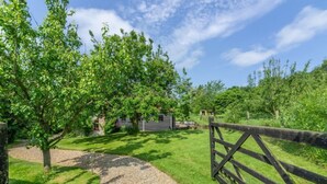 A rural property with a gravel path leading to a wooden gate, surrounded by lush greenery and a small building in the background. - Apple Tree Barn, Langham, Norfolk (Langham)