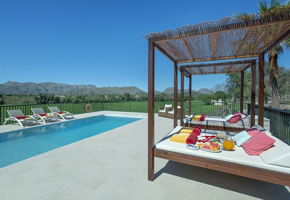 Un espace aménagé au bord de la piscine, avec des chaises longues, un lit avec des serviettes et une pergola.