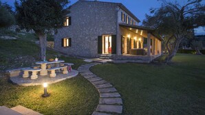 A stone house with a stone pathway leading to a circular seating area, a covered patio, and a well-maintained lawn. - VILLA SIQUIER - LUXURY RETREAT WITH MOUNTAIN VIEWS (Pollensa)