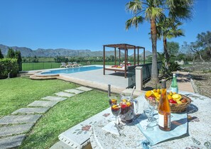 Une piscine avec des chaises longues, une pergola et une table où sont disposées des boissons et des fruits.