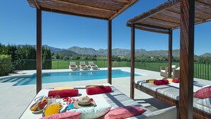 A poolside area with lounge chairs, a table with breakfast, and a view of mountains. - VILLA SIQUIER - LUXURY RETREAT WITH MOUNTAIN VIEWS (Pollensa)