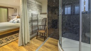 Ein Schlafzimmer mit einem Bett, einem Sessel, einer Dusche mit Glastür und Holzboden.