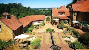 A courtyard with traditional architecture, featuring brick buildings with red-tiled roofs and a central garden area. - A spacious and luxurious retreat for couples near Great Tew (Chipping Norton)
