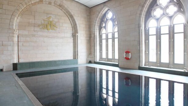 Ein großer, überdachter Schwimmbereich mit Rundbogenfenstern und einer Steinwand.