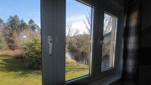 Ein Zimmer mit Fensterblick auf eine Rasenfläche und Bäume.