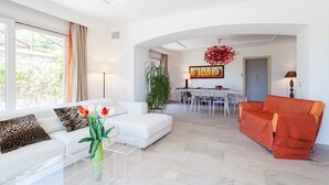 A modern living room with a white sofa, an orange sofa, a glass coffee table, and a dining area in the background. - Villa Yuri with private pool (Massa Lubrense)