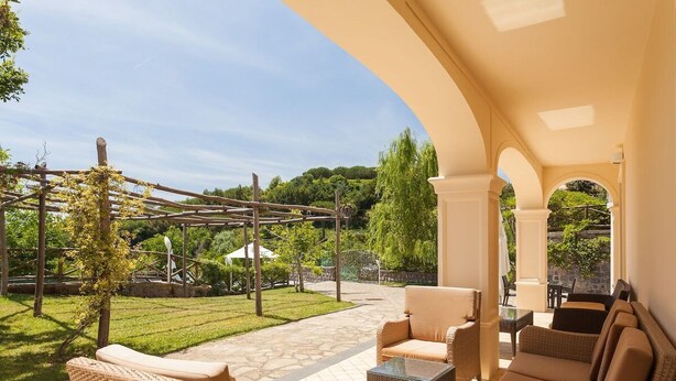 An outdoor patio with wicker furniture, a pergola, and a view of a landscaped garden. - Villa Yuri with private pool (Massa Lubrense)