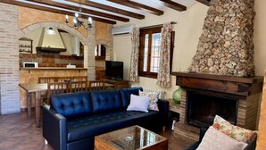 Una sala de estar con un sofá, una mesa de centro de vidrio, una chimenea y una zona de cocina con un televisor.