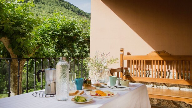 Una mesa al aire libre con vistas a un viñedo, un banco de madera y una pared de piedra.