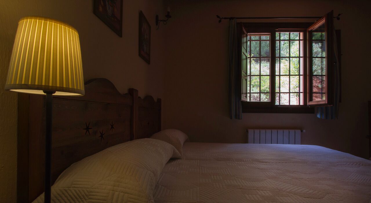 Une chambre à coucher avec une tête de lit en bois, un lit recouvert d’une courtepointe, une lampe sur pied et une fenêtre avec des rideaux.