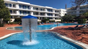 En swimmingpool med en fontän, omgiven av solstolar och en hotellbyggnad i bakgrunden.