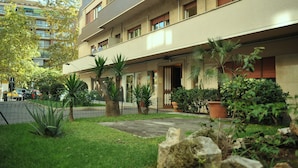 A multi-story hotel with a flat facade, balconies, and a well-maintained garden with various plants and a paved walkway. - 6 bedrooms, 3 bathrooms, 1 kitchen, 1 dining room, 5 minutes walk to the Vatican (Roma)