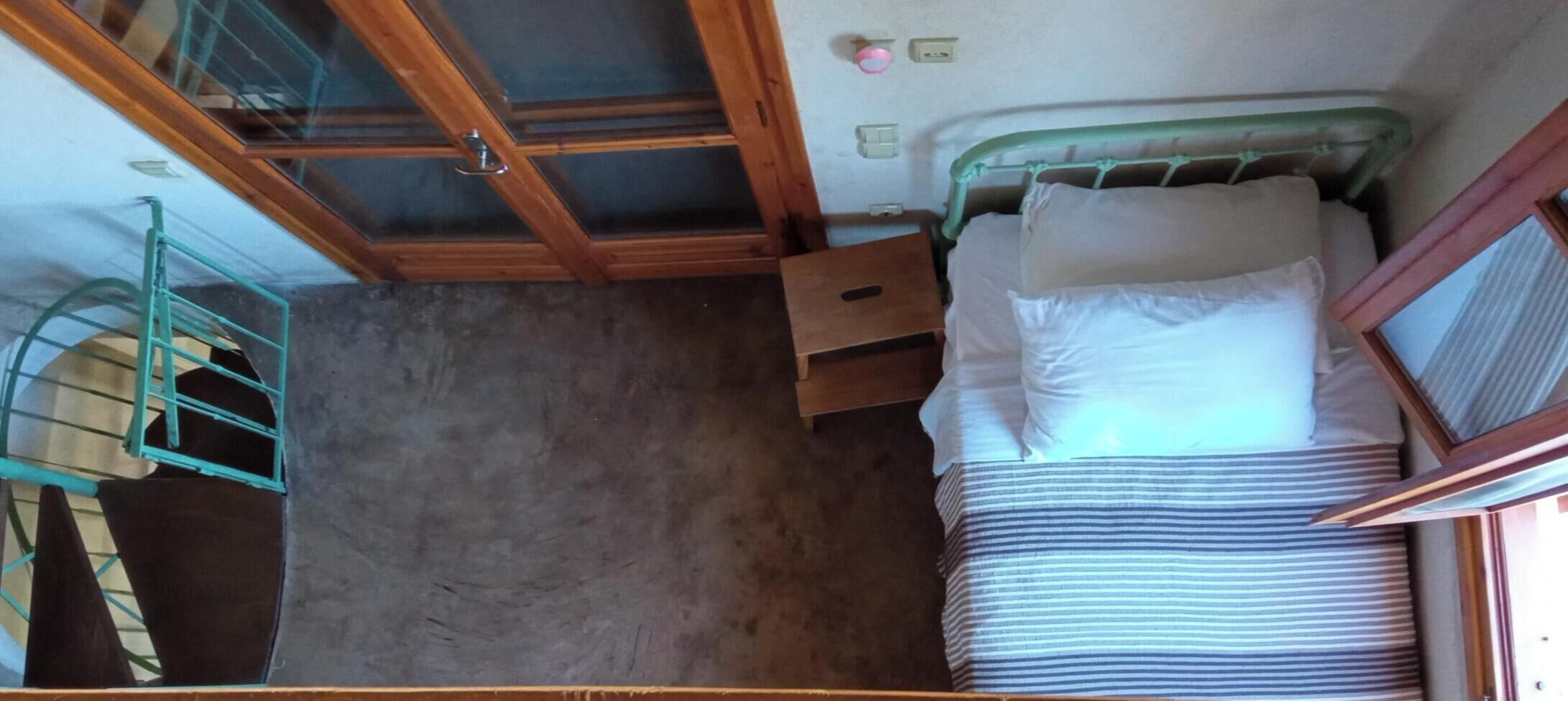 Habitació petita i senzilla amb un llit individual, un armari de fusta i una taula petita.