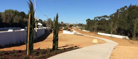 A paved pathway curving through a landscaped area with a white wall on one side and trees on the other.