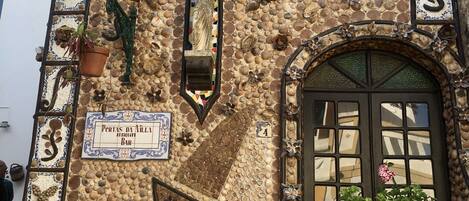 Une façade d’immeuble ornée d’une mosaïque de coquillages, d’une statue et d’une enseigne indiquant « Portas da Villa Bar ».