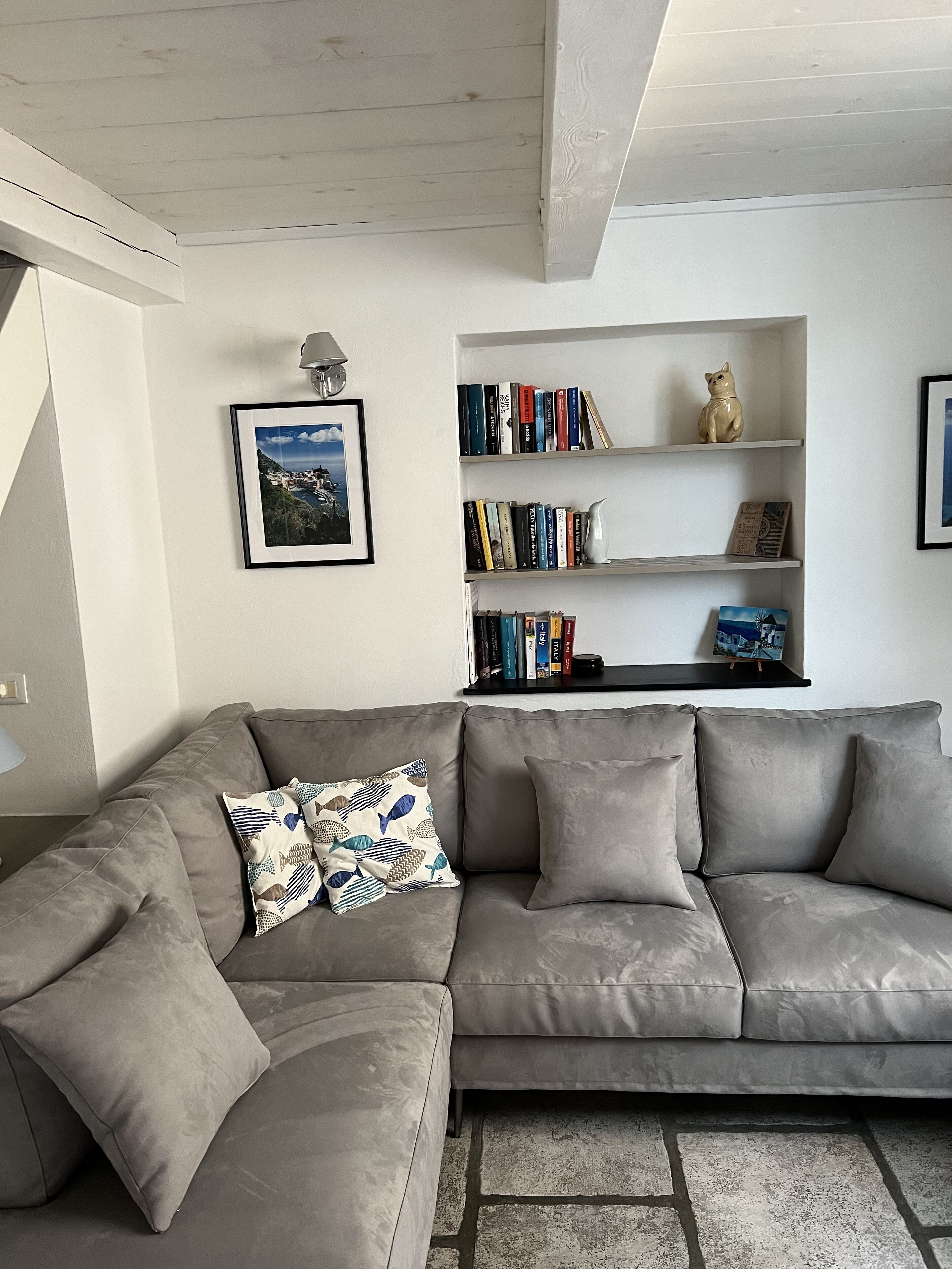 A modern living room with a grey sofa, a bookshelf with books and decorative items, a framed picture on the wall, and a lamp.