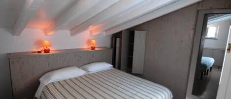 Un dormitorio con cama, dos lámparas de noche, cabecera de madera y una puerta que da a otra habitación.