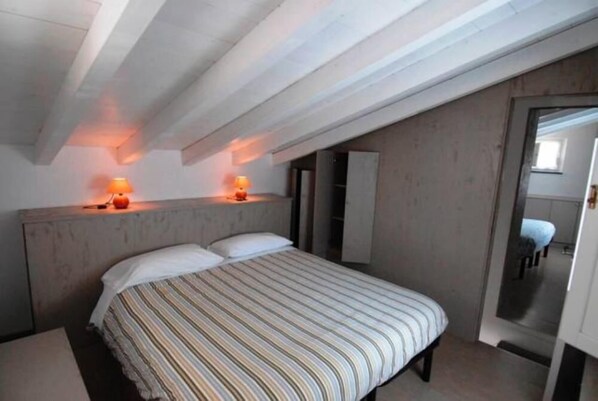 A bedroom with a bed, two bedside lamps, a wooden headboard, and a door leading to another room.