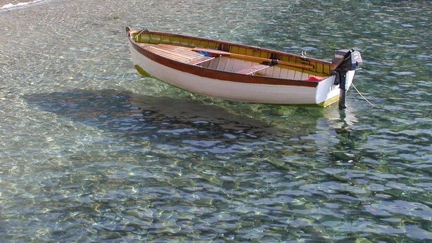 Una pequeña embarcación de madera con motor fueraborda Yamaha anclada en aguas poco profundas y transparentes cerca de una playa arenosa.