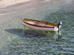 Een kleine houten boot met een Yamaha buitenboordmotor afgemeerd in helder ondiep water nabij een zandstrand.
