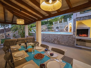 An outdoor dining area with a pool and stone walls, featuring a grill and lounge seating. - Villa Alcanada Sunrise. Your villa with private pool and sea views in Alcanada. (Alcúdia)