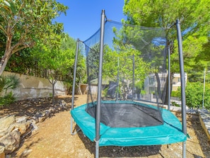 A trampoline with a safety net, surrounded by trees and a stone wall. - Villa Alcanada Sunrise. Your villa with private pool and sea views in Alcanada. (Alcúdia)