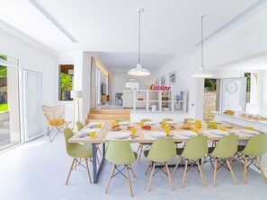 A modern dining area with a long table set for multiple people, surrounded by green chairs. - Villa Alcanada Sunrise. Your villa with private pool and sea views in Alcanada. (Alcúdia)