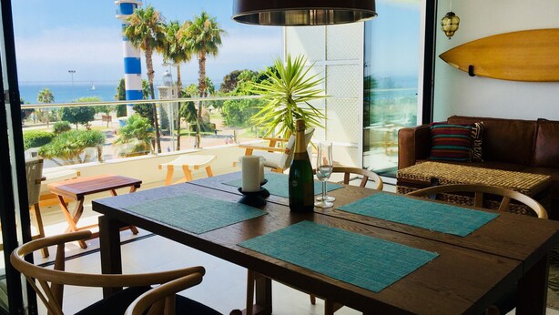 Un balcon avec vue sur la mer, une table avec des chaises, une planche de surf et un canapé.