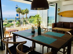 Un balcon avec vue sur la mer, une table avec des chaises, une planche de surf et un canap é.