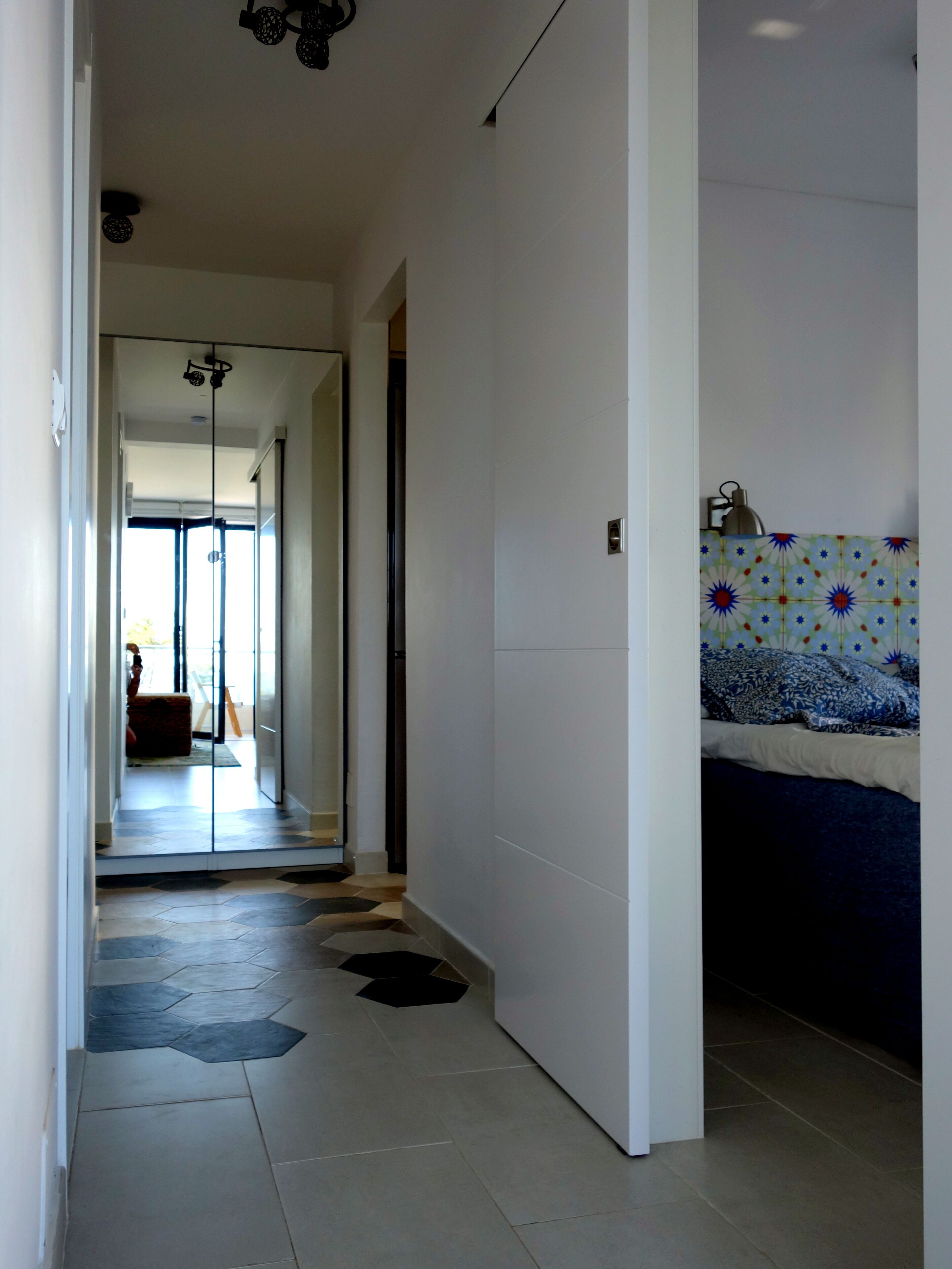A hallway with a tiled floor, a bed with a patterned headboard, and a wall with decorative tiles.
