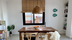 Un coin repas avec une table en bois, des chaises et une grande fenêtre équipée de stores.