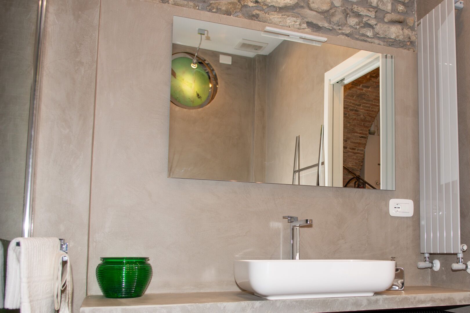 A bathroom with a large mirror, a white sink, a green vase, and a towel rack.
